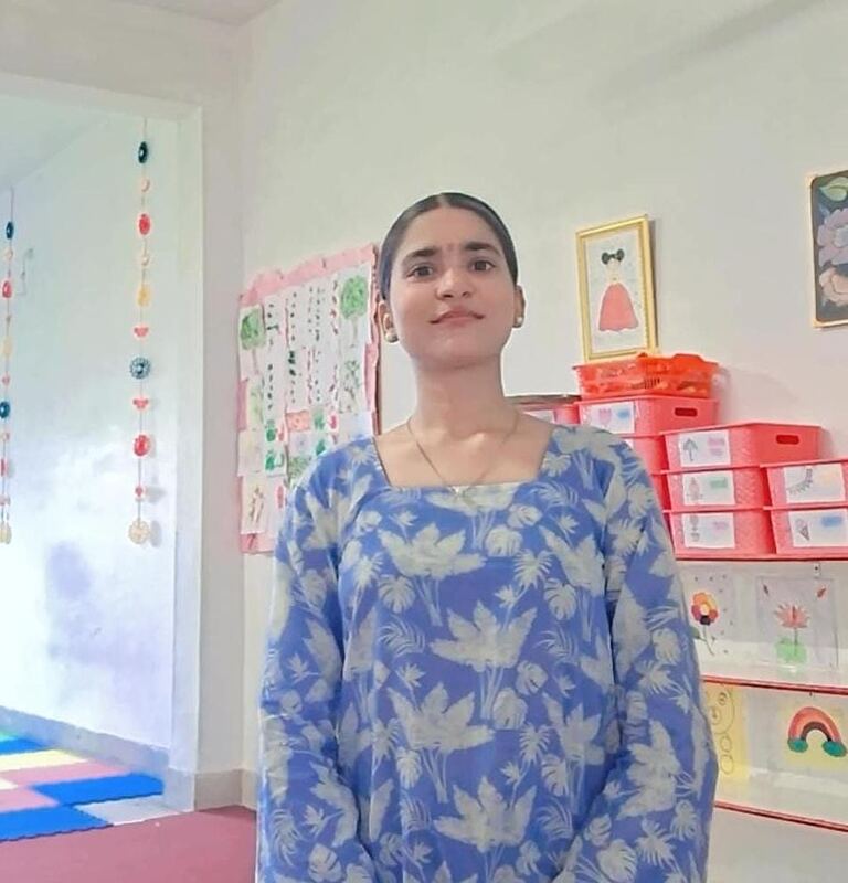 Ruby, standing in the classroom in front of the children's paper work on the wall.