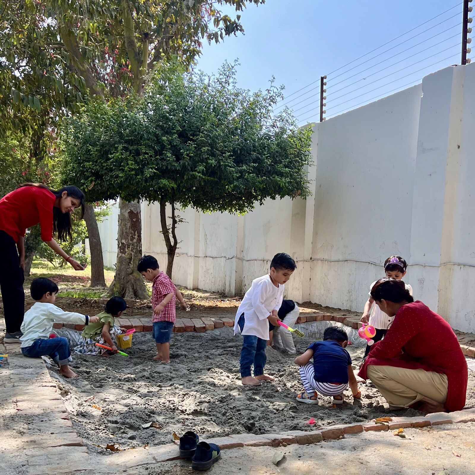 Children and two adults digging in the sandpit under a tree.